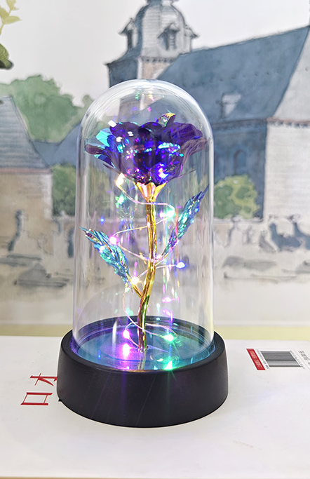 Decorative rose in a glass dome with colorful lighting on a white surface.