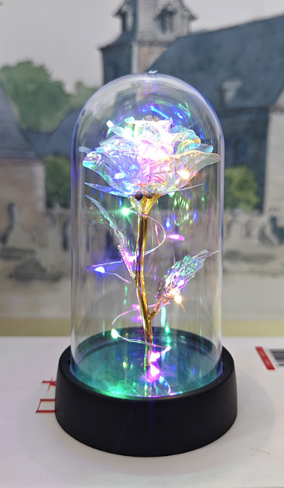 Decorative LED rose in a glass dome on a white surface with a blurred background