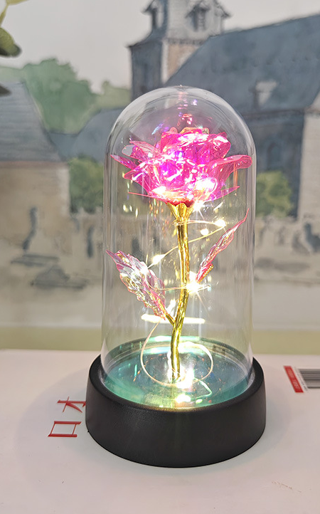 Decorative lighted flower in a glass dome on a table with a blurred background