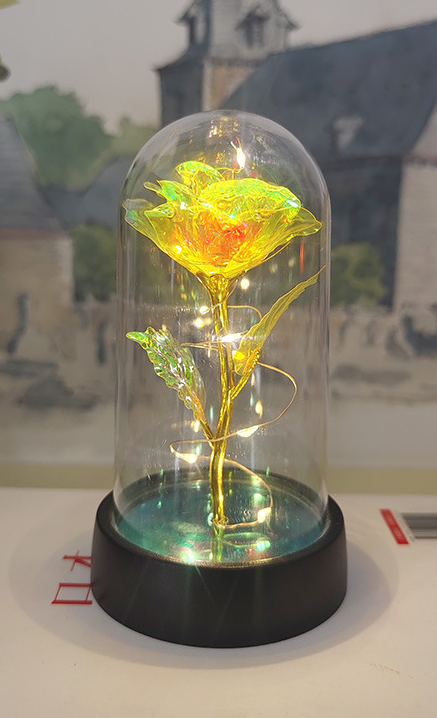 Gold rose inside a glass dome on a black base with a blurred background