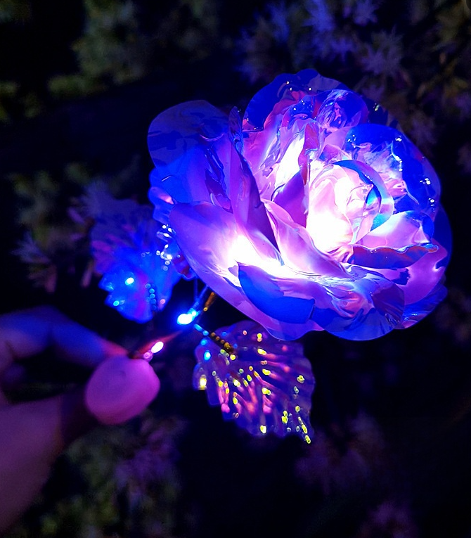 Decorative LED rose with colorful lights held by a hand against a dark background